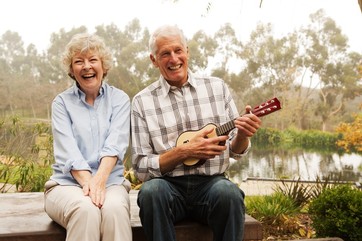 Husband playing the ukulele with wife by lake