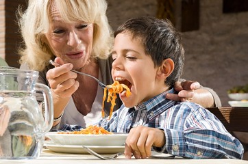 Grandmother feeding pasta to grandson